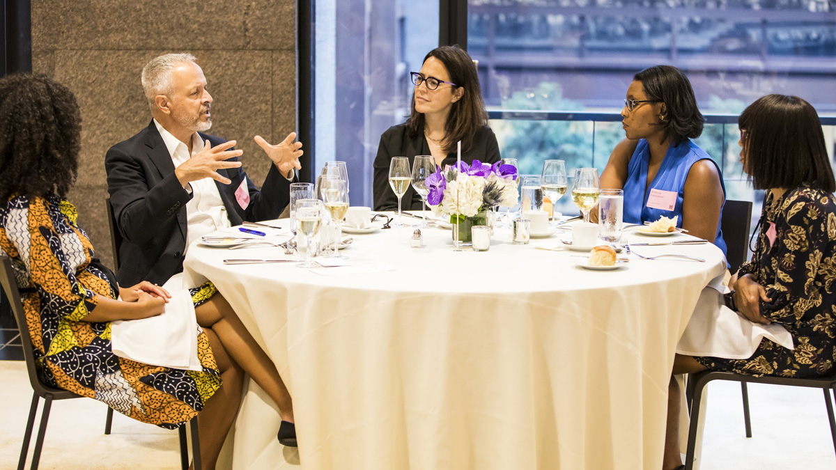 Five people seated around a round dining table with a floral centerpiece.